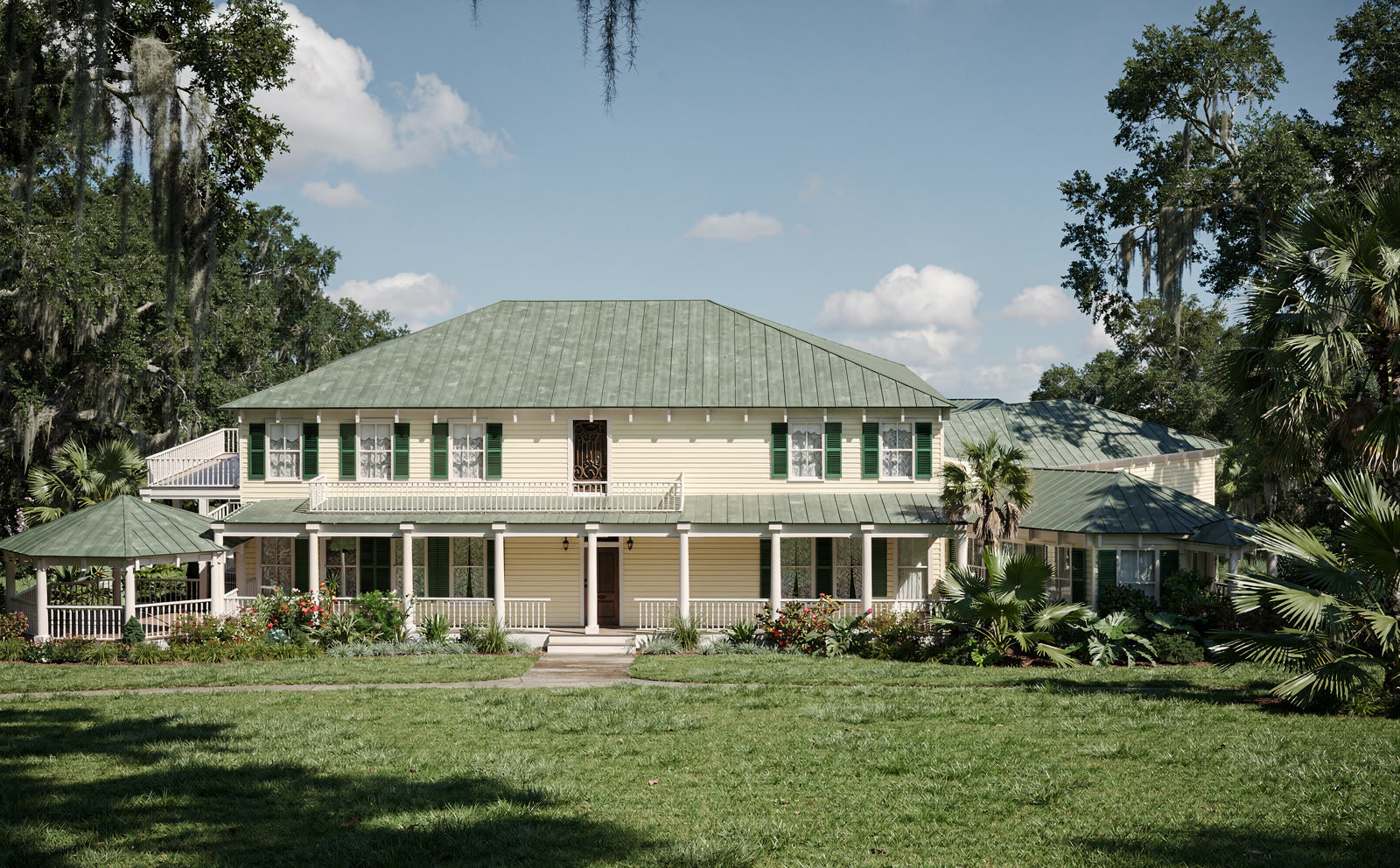 Photograph of a two story cream clapboard house with a green
      standing seam hipped roof, a full width porch on turned posts with a white balustrade, dark green louvered
      shutters, an octagonal gazebo at the left and a wing at the right, on a mown lawn under live oaks with
      Spanish moss.