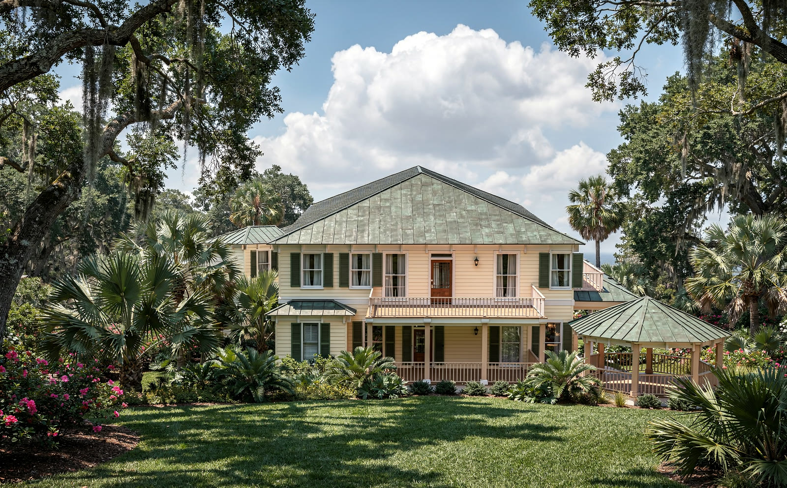 Photograph of the same house from the west: the gazebo end nearest
      the camera, the two story porch running away to the right, palms and azalea beds against the foundation.